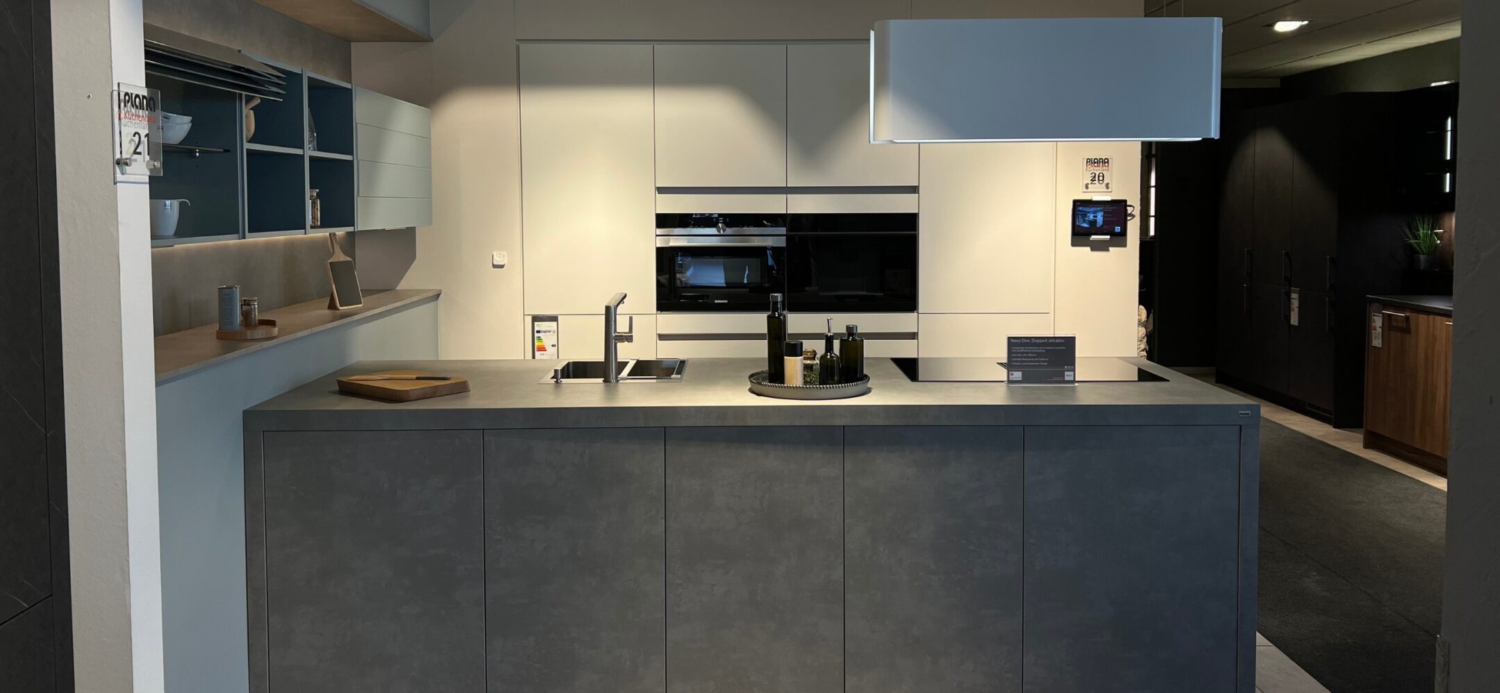 Kompakte Inselküche in Betonoptik und weißer griffloser Küchenzeile bei PLANA in Ravensburg