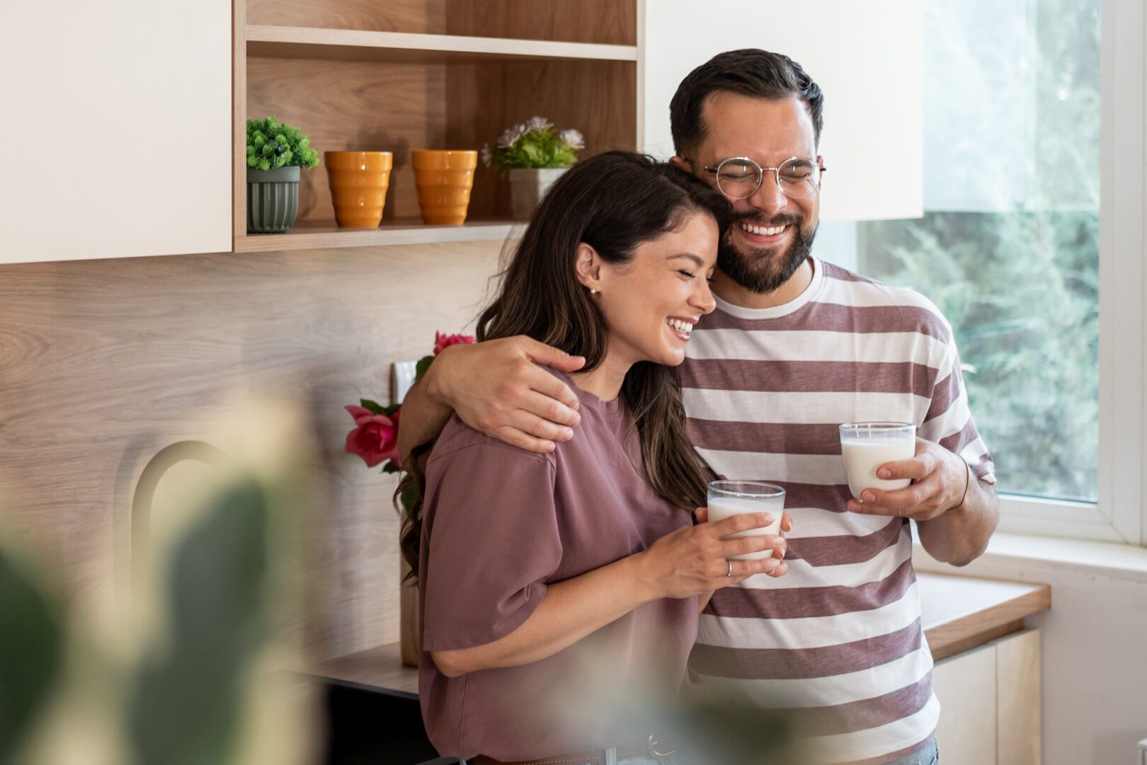 Ein Paar genießt ein Glas Milch in einer modern gestalteten Küche, Mann legt Arm um Frau