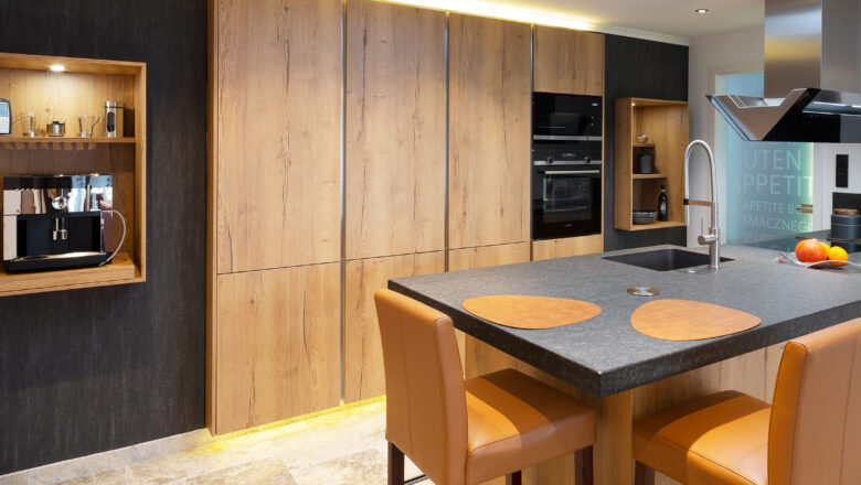 PLANA Küchenstudio Hilden moderne Inselküche mit grifflosen Fronten in Holzoptik sowie gemütlicher Sitzgelegenheit