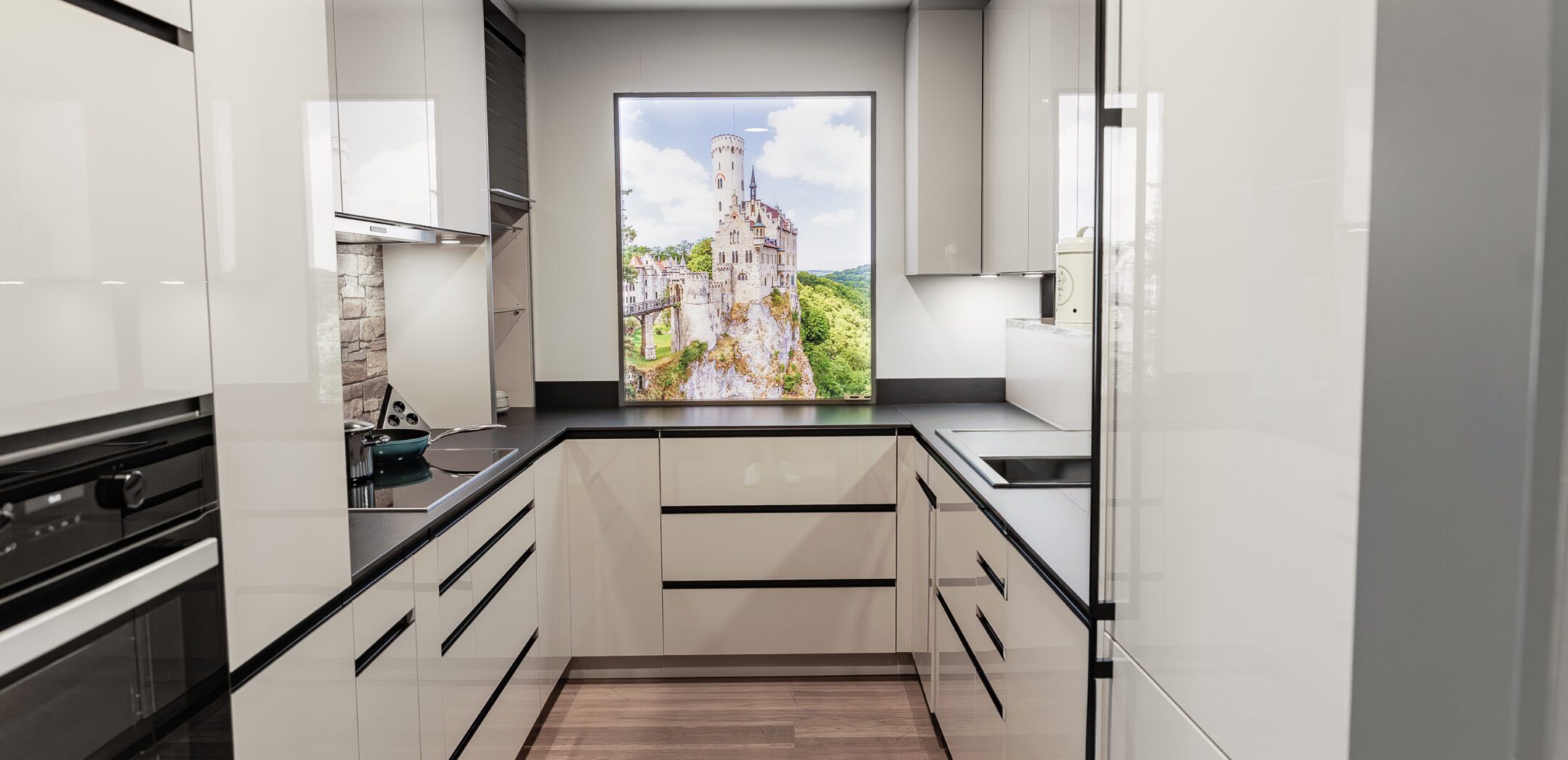 U-förmige Küche in Beige mit beleuchtetem Rückwand-Motiv von Schloss Lichtenstein.