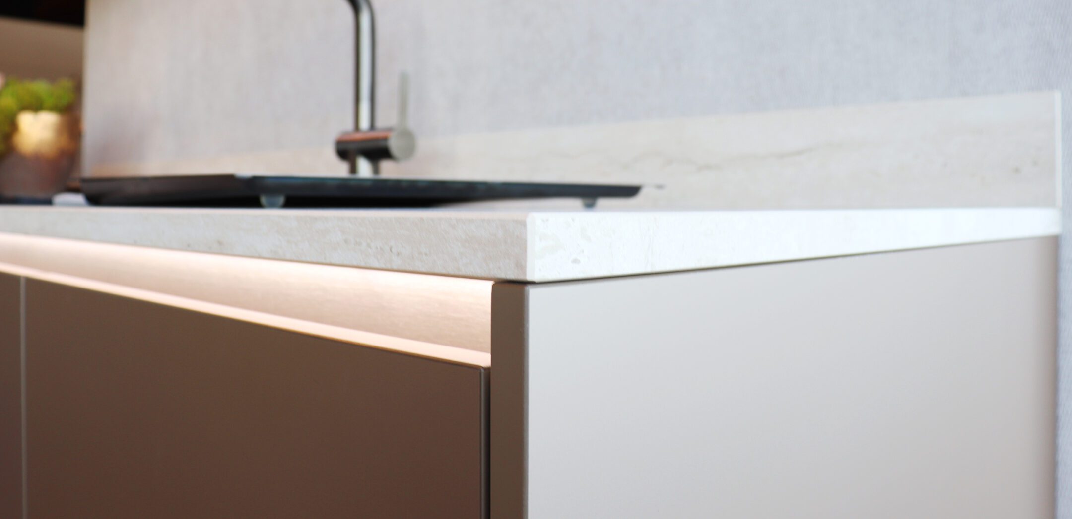 Detailansicht einer hellen Naturstein-Arbeitsplatte mit integrierter LED-Griffleistenbeleuchtung.