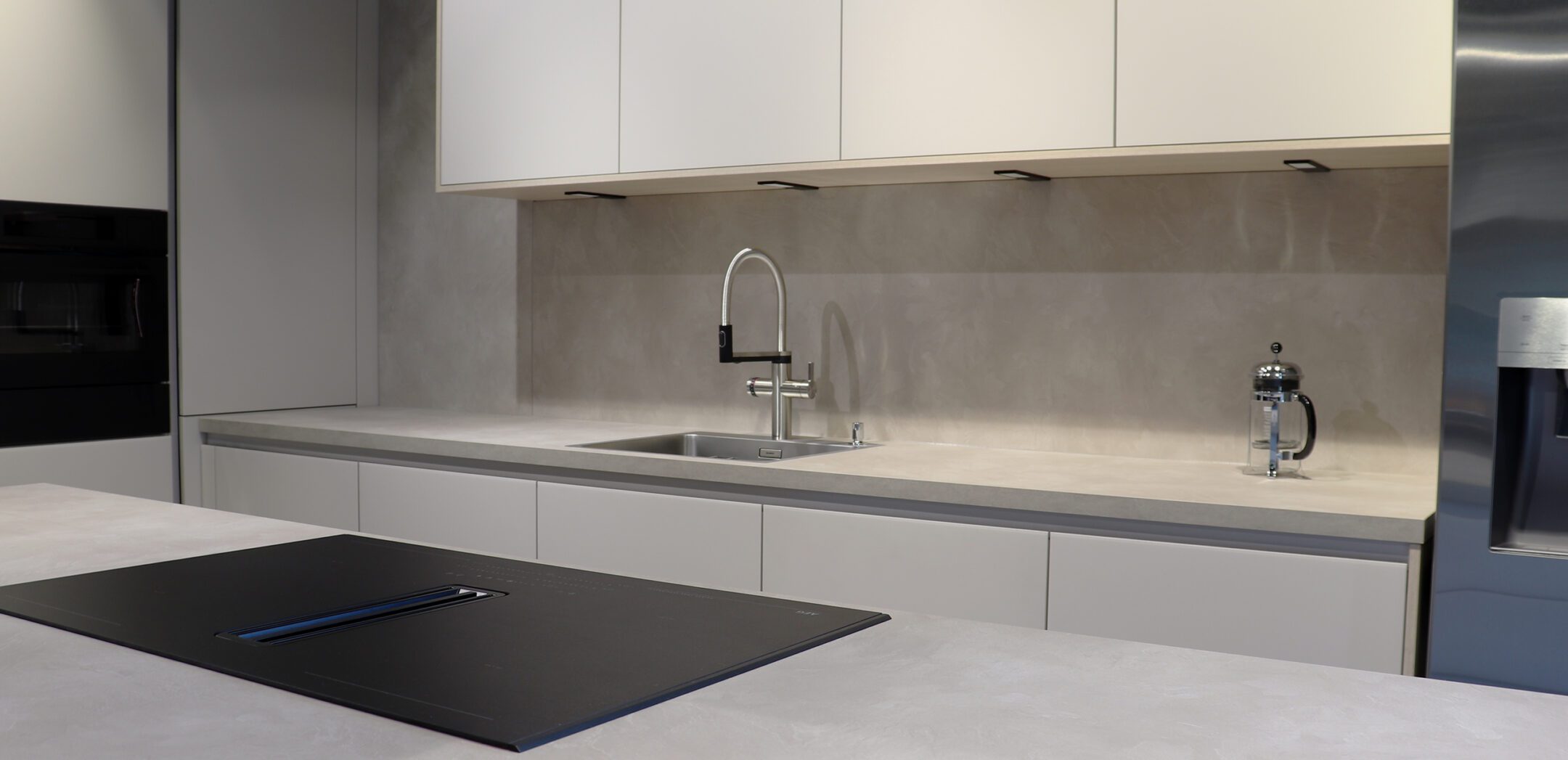 Moderne weiße Einbauküche mit Beton-Optik Arbeitsplatte und minimalistischem Spülbecken.