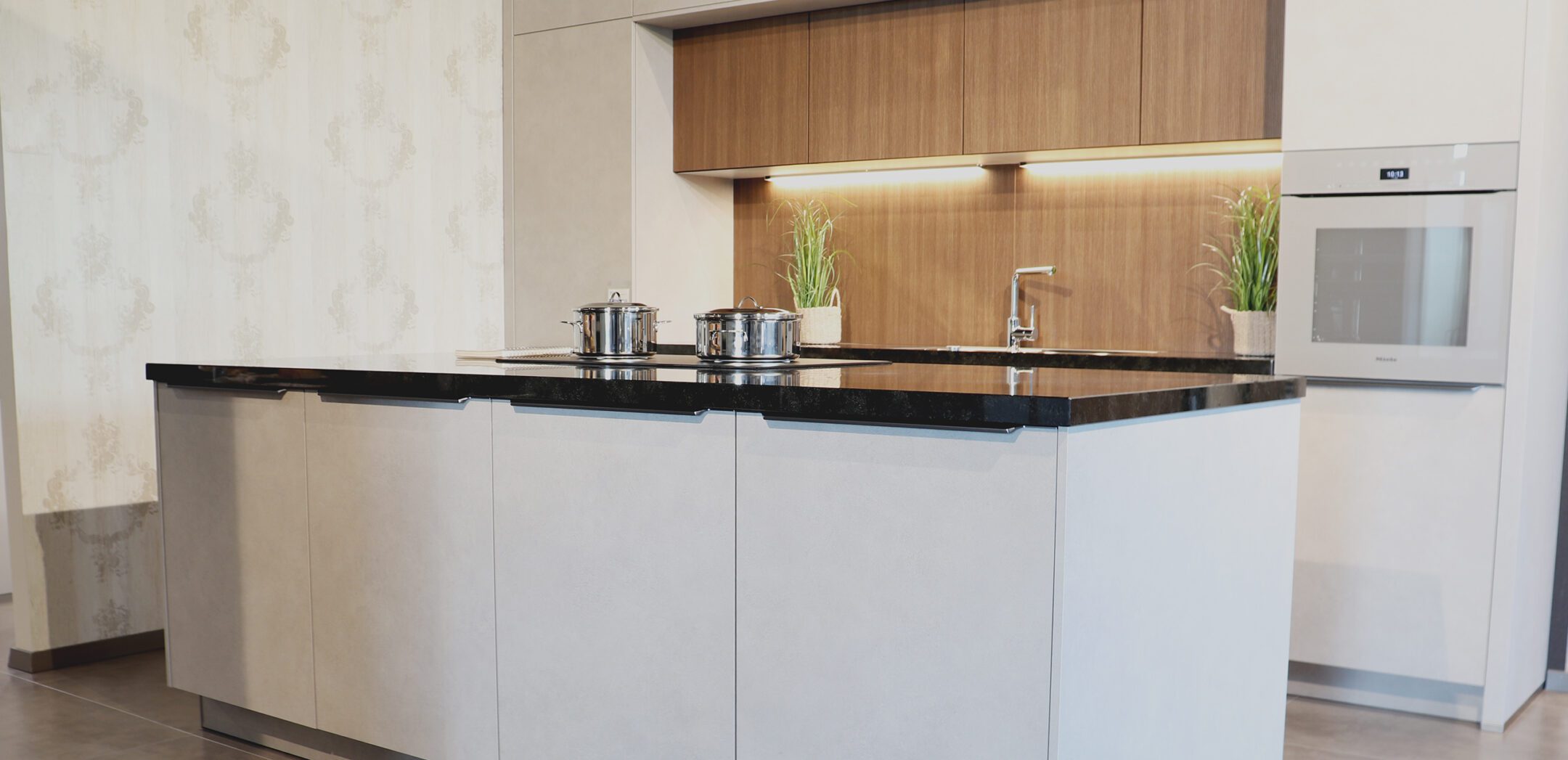 Moderne Kücheninsel in Grau-Beton-Optik mit schwarzer Arbeitsplatte und integriertem Backofen in der Rückwand.