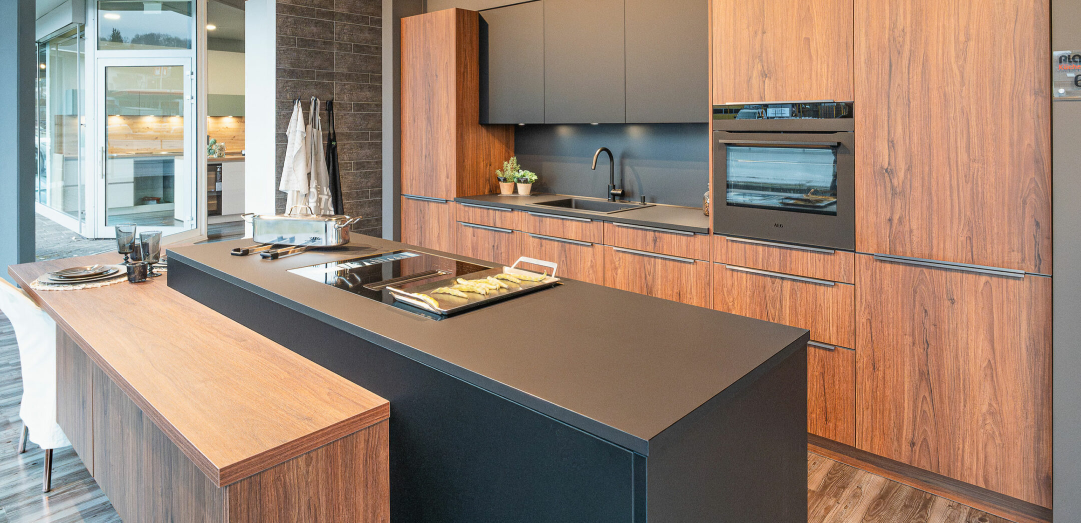 Inselküche mit Fronten in warmen Holztönen und dunkler Arbeitsplatte