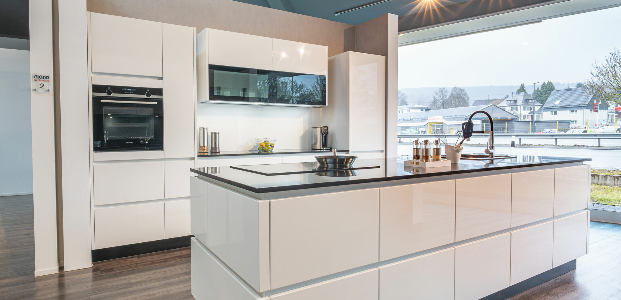 Hochwertige grifflose Inselküche mit weißen Glanzlack-Fronten und dunkler Arbeitsplatte