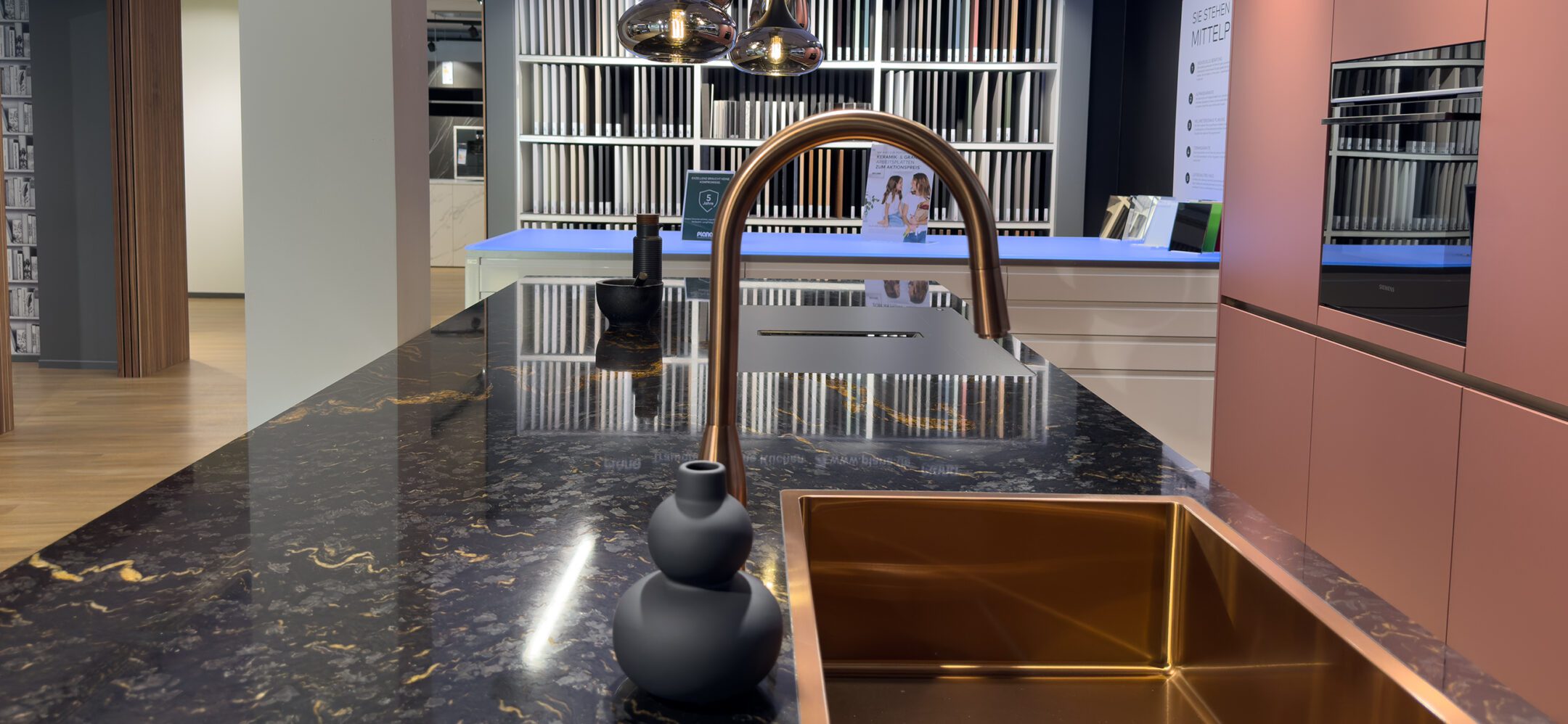 Granit-Arbeitsplatte mit mattem flächenbündigen Kochfeld, Spüle Armatur in Gold bei PLANA Sinzheim