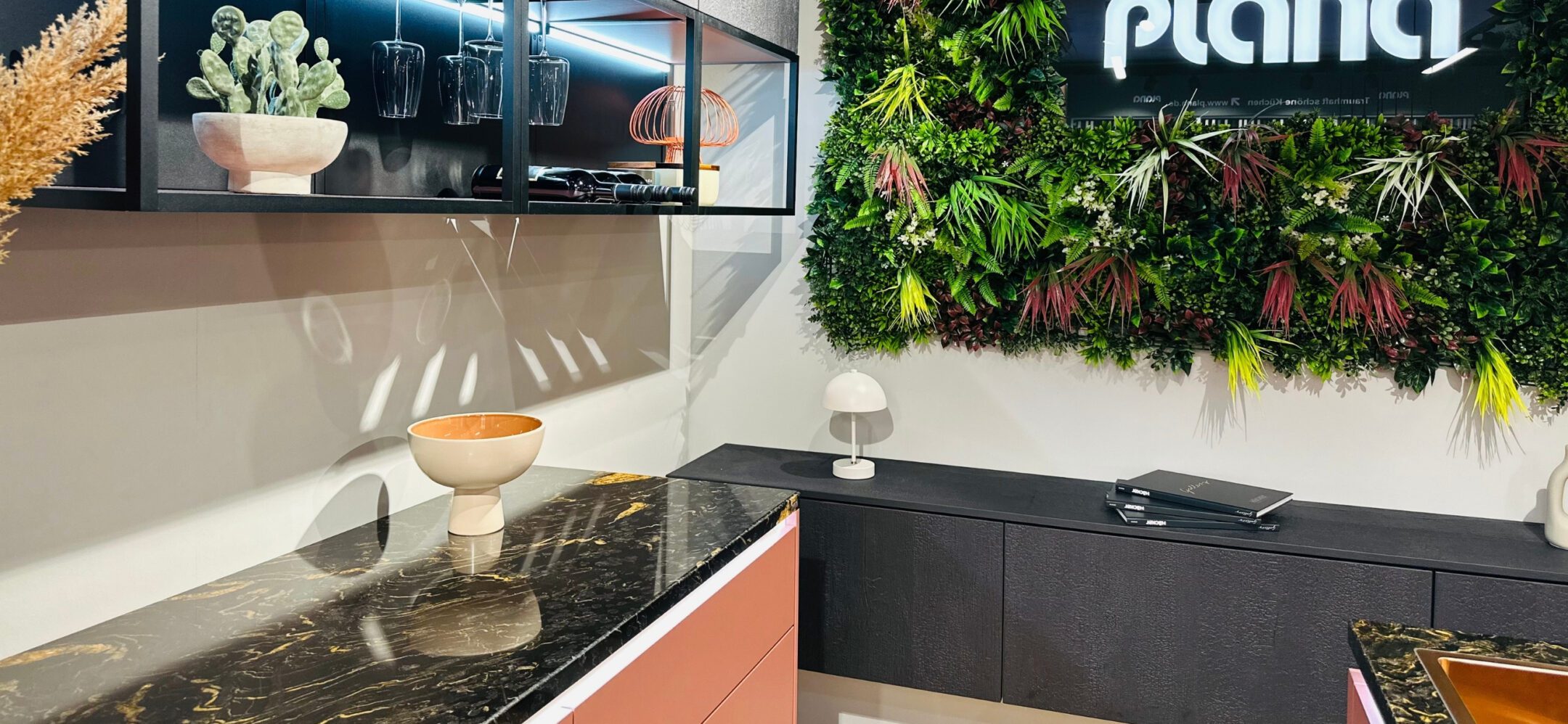 Moderne Küchenplanung mit lachsfarbenen Unterschränken, schwarzer Marmor-Arbeitsplatte und vertikalem Garten.