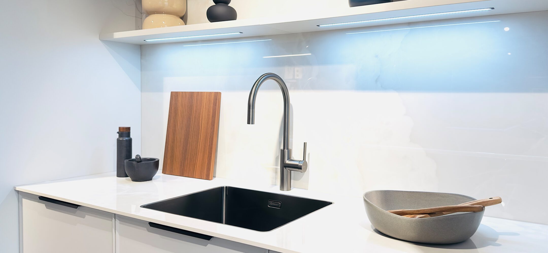 Edelstahl-Küchenarmatur mit hohem Auslauf über einer schwarzen Unterbauspüle von Caressi.