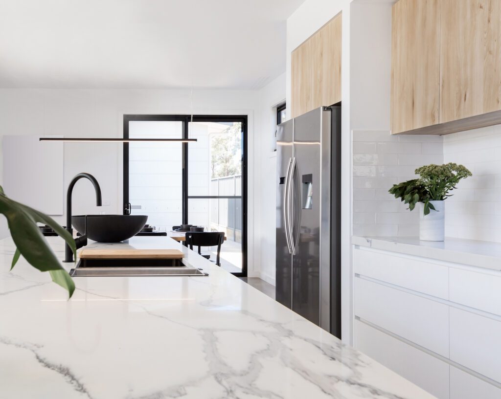 Perspektivische Ansicht einer hellen Design-Küche mit Kochinsel, schwarzen Akzenten und Blick in den Garten.