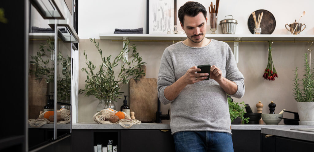 Mann steht mit Smartphone in Küche