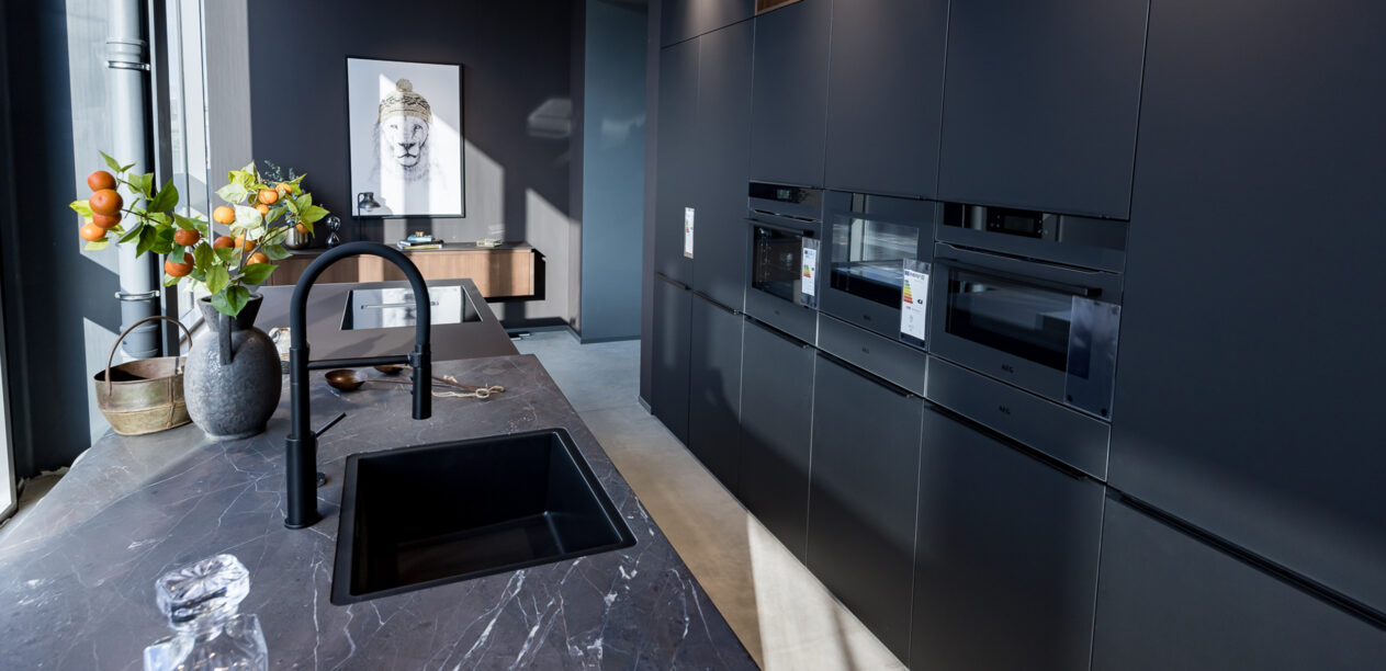 Schwarz matte Inselküche mit Granitarbeitsplatte und schwarzer Spüle und Armatur im PLANA Küchenstudio Niederzier