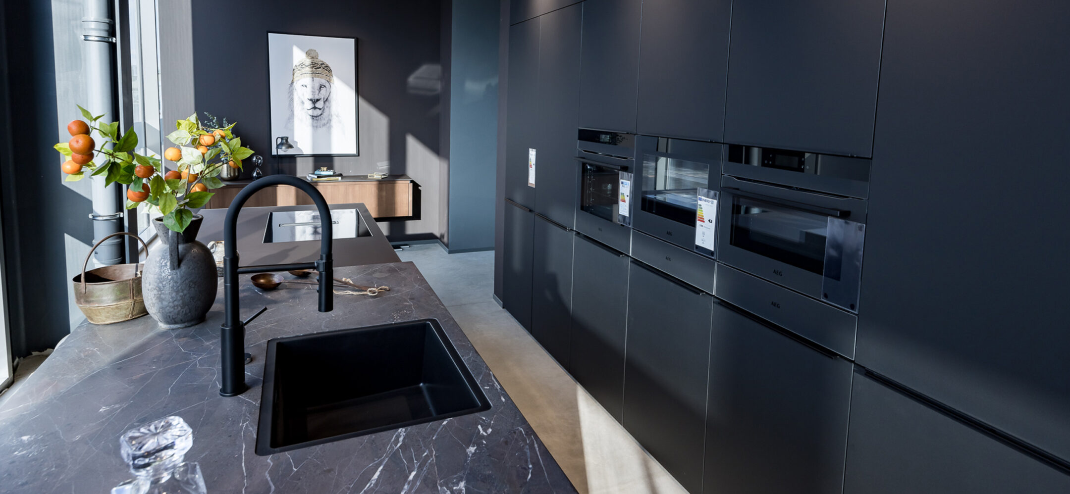 Schwarz matte Inselküche mit Granitarbeitsplatte und schwarzer Spüle und Armatur im PLANA Küchenstudio Niederzier