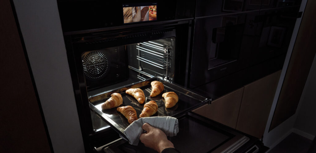 Ein Mann nimmt frische Croissants aus einem Siemens Backofen