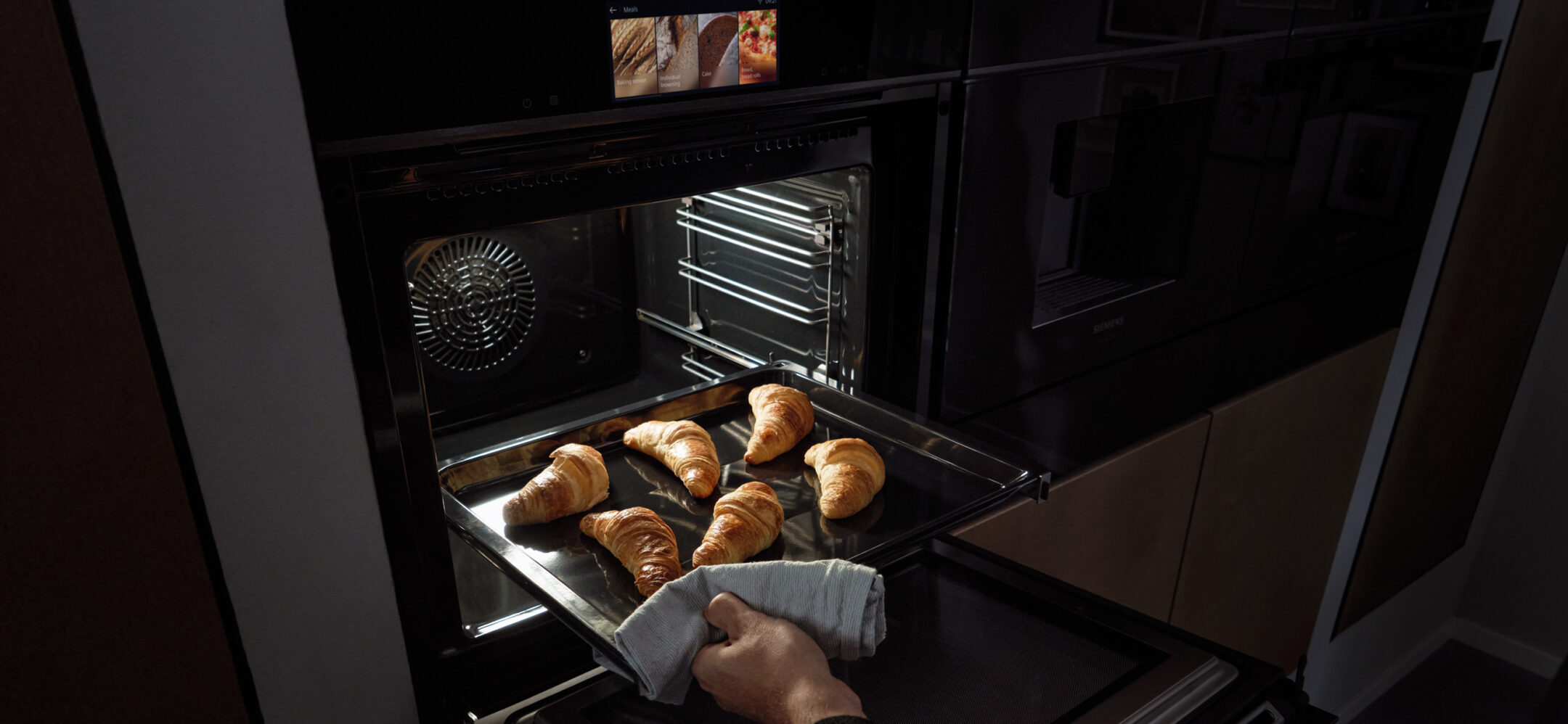 Ein Mann nimmt frische Croissants aus einem Siemens Backofen