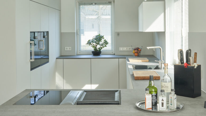 PLANA Küchenstudio Lippstadt Kundenküche mit weißen grifflosen Fronten mit grauer Stein-Arbeitsplatte, hochwertigen Einbaugeräten und Teppanyaki-Kochfeld