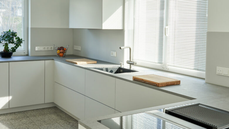 PLANA Küchenstudio Lippstadt Kundenküche mit weißen grifflosen Fronten mit grauer Stein-Arbeitsplatte, hochwertigen Einbaugeräten und Teppanyaki-Kochfeld