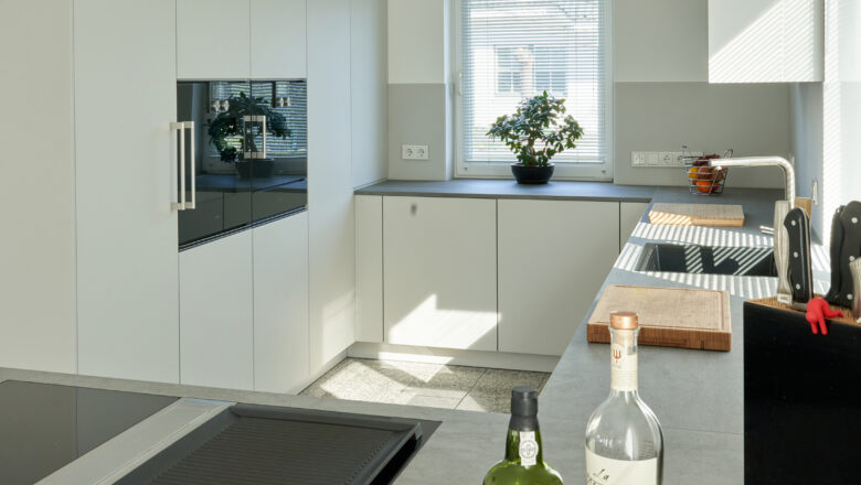 PLANA Küchenstudio Lippstadt Kundenküche mit weißen grifflosen Fronten mit grauer Stein-Arbeitsplatte, hochwertigen Einbaugeräten und Teppanyaki-Kochfeld
