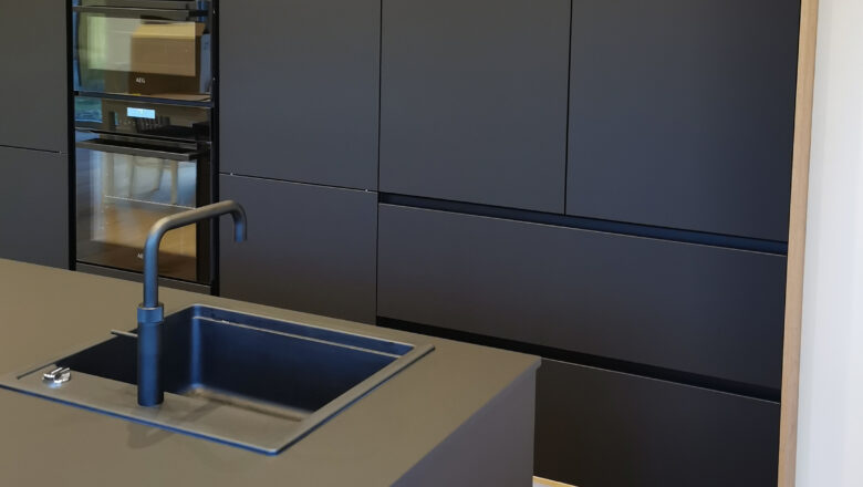 PLANA Küchenstudio Lippstadt Kundenküche mit schwarzen grifflosen Fronten, hochwertigen Einbaugeräten und dunkler Arbeitsplatte