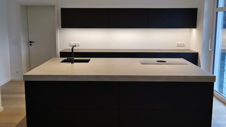 PLANA Küchenstudio Lippstadt dunkle Inselküche mit grauer Steinarbeitsplatte und hochwertigen Einbaugeräten