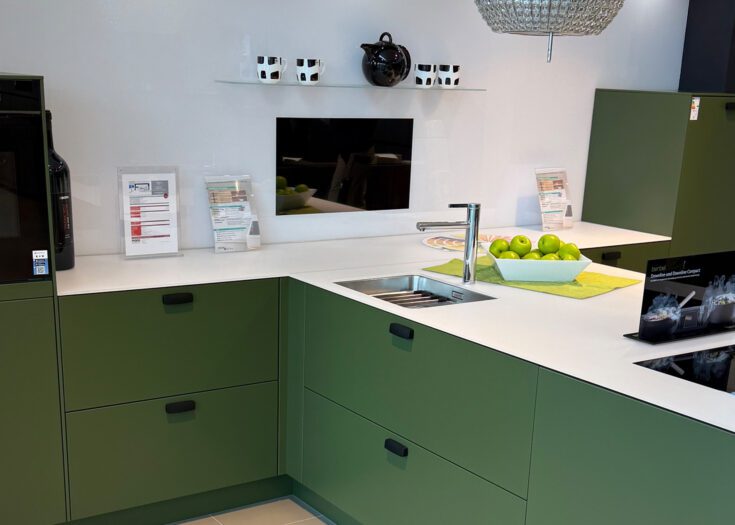 PLANA Küchenausstellung Hilden Olivgrüne Küche in T-Form mit weißer Glas-Arbeitsplatte