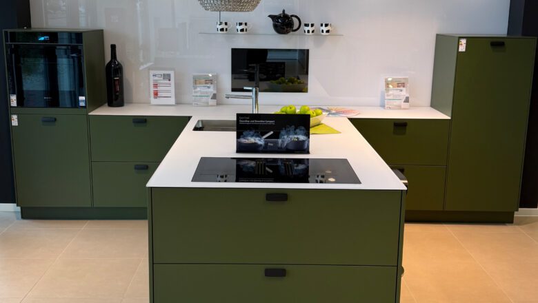 PLANA Küchenausstellung Hilden Grüne Küche mit weißer Glas-Arbeitsplatte und Induktionskochfeld