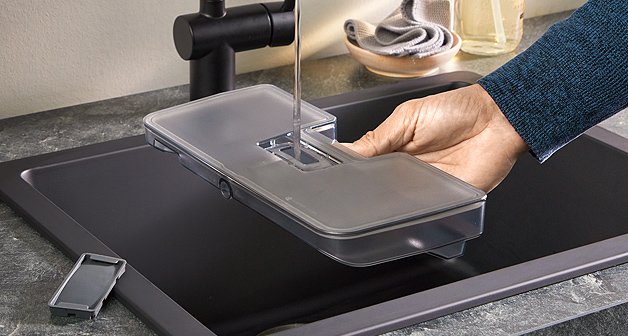 Mann füllt Wassertank vom Dampfbackofen an einem schwarzen Spülbecken