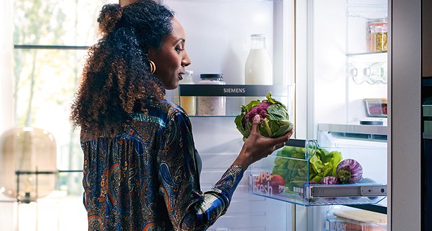 Frau steht am offenen Kühlschrank und holt einen Rotkohl aus dem Fresh-Fach