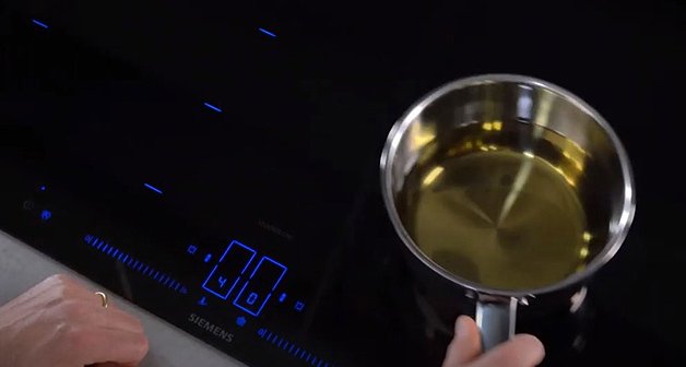 Schwarzes Siemens Induktions-Kochfeld mit blauem Touch-Display und Topf mit gelber Flüssigkeit