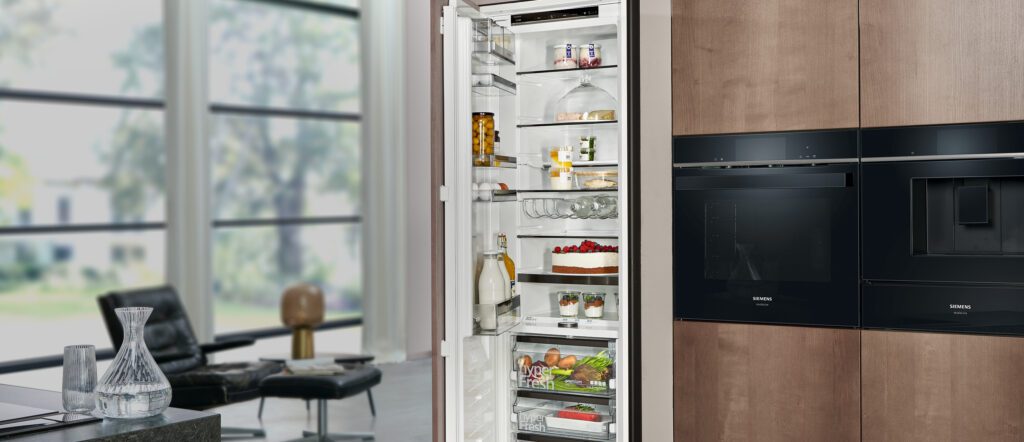 Küchenzeile mit offenem voll eingeräumten Kühlschrank, Backofen und Einbaukaffeemaschine
