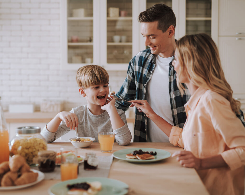 Eine glückliche Familie frühstückt gemeinsam in einer hellen Landhausküche.