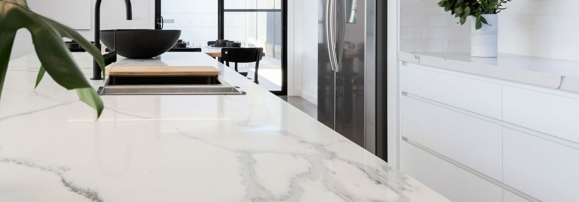 Detailaufnahme einer weißen Marmor-Kücheninsel mit schwarzer Armatur und Side-by-Side Kühlschrank.