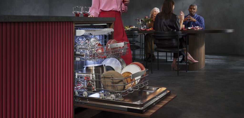 Eingeräumte Spülmaschine von AEG mit Menschen am Esstisch im Hintergrund