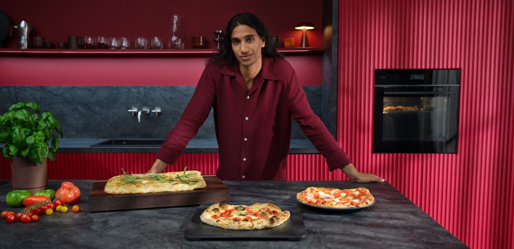 Mann steht an Kücheninsel mit 3 verschiedenen Pizzavariationen