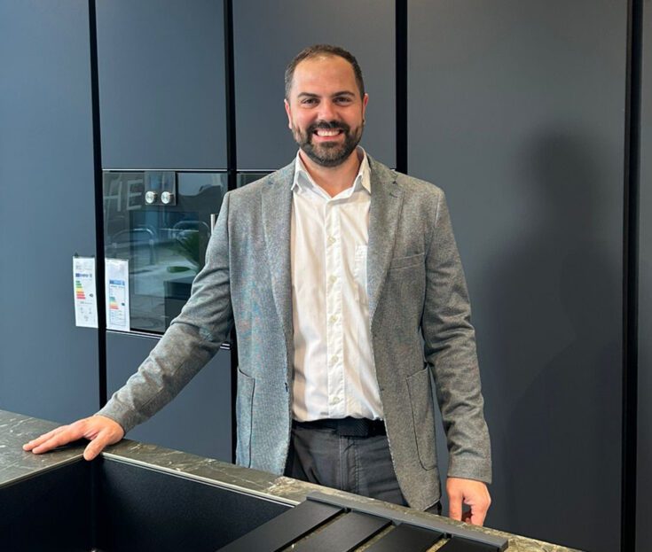 Ein Küchenexperte steht lächelnd an einer dunklen Spüle im Showroom.