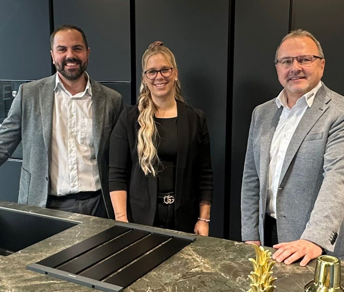 Drei lächelnde Küchenberater stehen gemeinsam an einer modernen Kochinsel.