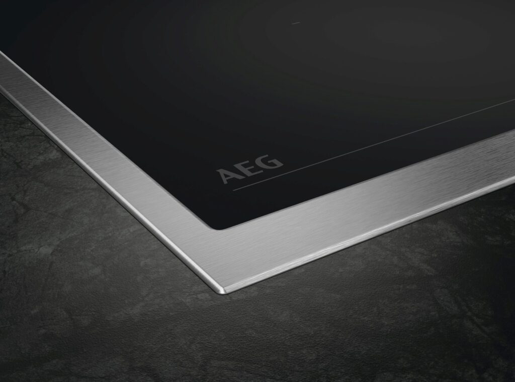 Nahaufnahme eines AEG Induktionskochfelds mit umlaufendem Edelstahlrahmen und dezentem Logo-Print.