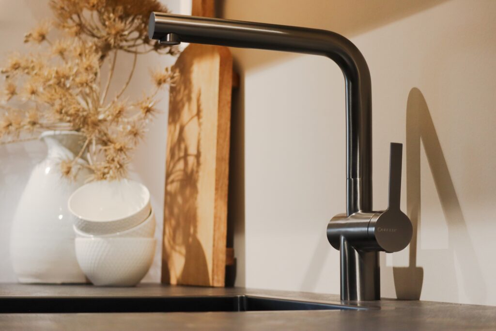 Moderne Küchenarmatur Caressi CA1108GMUECO in Gunmetal-Optik neben weißen Schüsseln.