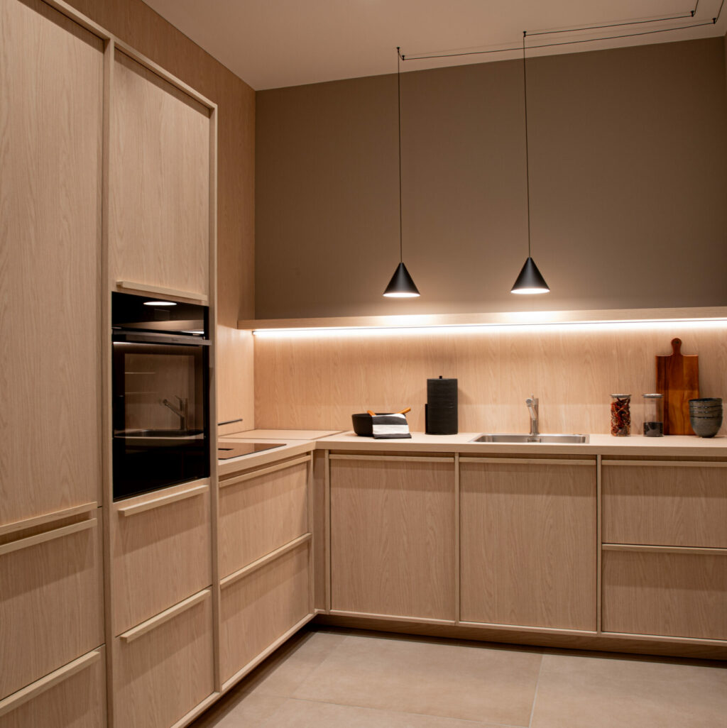 Moderne L-förmige Holzküche im minimalistischen Japandi-Stil, beleuchtet mit Einbaustrahlern und Pendelleuchten.